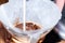 White milk pouring on brown ground coffee in paper filter in glass jar