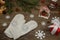 White mittens with a snowflake made of rhinestones on a background of Christmas toys, a gingerbread house and fir branches