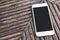 A white mobile phone with blank black desktop screen on vintage wooden table background