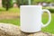 White mockup coffee or tea mug on standing on stone outdoors. Nature background with green trees grass. Summer spring. Blank space