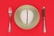 A white model of the human brain lies in a plate on a red background, next to a fork and knife.