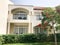 A white modern cottage, a villa, a house, a building with windows and a balcony and a green tree with red flowers, a royal delonis