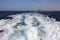 The white moving wake of the sea waves in the blue water caused by the sailing pace of a boat or a yacht or ship between the