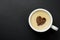 White mug of cappuccino, on a black background with copy space. A chocolate heart in the center of a cup of hot coffee drink