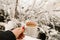 White mug of coffee with milk in the girl`s hand on the snowy background, winter concept photo.