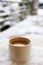 White mug of coffee with milk on a snowy table.