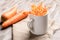 White mug with longitudinal carrot chips on beige fabric and two whole carrots on wooden table.