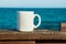 White mug, mock up, empty space for artwork, text, standing on wood plank, turquoise sea, clear blue sky