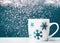 White mug with snowflakes on table at blue background with bokeh, front view concept. Winter holidays