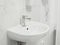 White new clean simple sink with metal shiny valve faucet in white interior of a medical clinic. Tiled wall in background