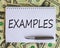 White note with inscription `examples` on beautiful background from dollar bills and metalic pen. Business concept