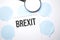 White noteapad and magnifier on blue speech bubles. Text Brexit. Business concept