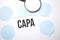 White noteapad and magnifier on blue speech bubles. Text capa. Business concept