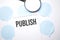 White noteapad and magnifier on blue speech bubles. Text Publish. Business concept