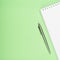 White notebook with steel pen on a green background. Office, save space, mock up, template, top view, flat lay.