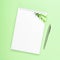 White notebook with steel pen and green branches on a green background. Office, spring composition, save space, mock up