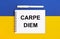 A white notebook with the text CARPE DIEM and a white pen on a blue and yellow background