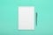 White notepad with steel pen on a turquoise background. Office table, minimal composition, copy space, mock up, template