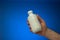 White opaque plastic bottle held in hand by Caucasian male. Close up studio shot,  on blue background