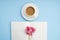 White open notebook for notes, white cup of coffee with milk, pink flower on a blue background, place for text, copy space. Top vi