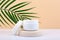 White opened cosmetic jar on beige podium against beige background with palm leaf. Concept of cosmetic products