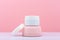 White opened cosmetic jar on pink podium against bright pink background with copy space