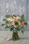 White and orange bridal bouquet of roses, freesia and eucalyphus on a gray textural background.