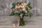 White and orange bridal bouquet of roses, freesia and eucalyphus on a gray textural background.