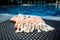 A white and orange Turkish peshtemal / towel and white seashells on rattan lounger with blue a swimming pool as background.