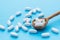 White oval pills in a wooden spoon on a blue background. Uncontrolled use of drugs in large quantities