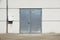 White Overhead Steel Garage Door On Exterior Of Beige Metal Building With Red Bumper Posts