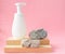 White packaging with a dispenser stands on a wooden stand and natural stones on a pink pastel background. Spa care concept, layout