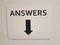 White paper answers sign with black down arrow on wall