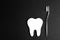White paper tooth with toothbrush on black background.