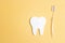 White paper tooth with toothbrush on yellow background. Dental health concept. Dentist day concept