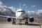 White passenger airplane with air-stairs at the airport apron on the background of high scenic mountains