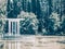 White pavilion with columns standing on a semicircular platform near a pond surrounded by tall trees arboretum