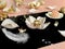 White pearl jewelry gold rings on a black background with pink opal in seashell , precious stones, rose petals and feathers concep