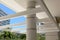 White pergola at the entrance to a building. In the background blue sky and vegetation.