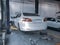 A white Peugeot 408 was lifted up by a lift in the workshop. All four wheels were removed for maintenance.