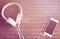 White phone and headphones flat lay on wooden table. Warm pink light toned photo.