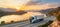 White pickup truck driving on a picturesque road with a stunning sunset in the background