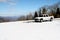 White pickup truck sitting on top of a snow covered mountain with beautiful sky and view of other mountains in the distance