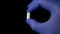 White pill in hand in blue medical protective gloves on a black background closeup.