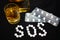 White pills on black background, which forming the word SOS, with glass and bottle of alcohol.