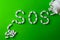White pills on green background, which forming the word - SOS, with a blister of pills on background.