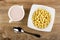 White pitcher with fruit yogurt, corn balls in bowl, spoon on wooden table. Top view