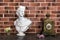 White plaster bust sculpture portrait of a young man and old clock on the table, details of luxury interior in classic