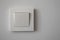 White plastic light switch on light gray wall, close-up