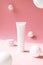 White plastic tube for cosmetic product on pink background with abstract white spheres, front view. Containers for eye moisturizer